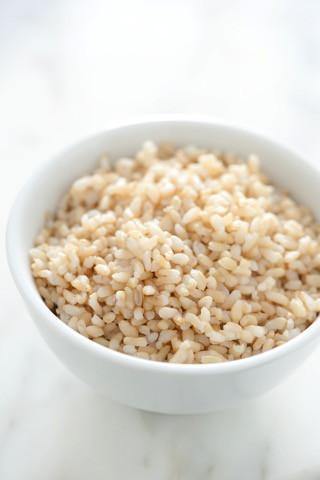 Bowl of cooked brown rice on a white marble surface, healthy whole grain food
