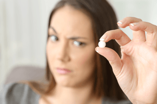 Woman with concerned expression holding a white supplement pill between fingers