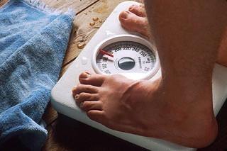 Person standing on analog bathroom scale next to blue towel, measuring body weight