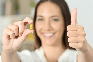 Woman holding a supplement capsule and showing a thumbs up, promoting brain health nutrients