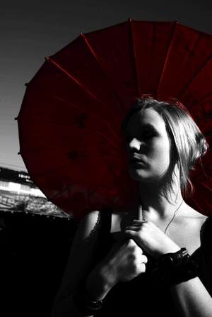 Woman holding red parasol, standing outdoors, dramatic lighting with shadowed face