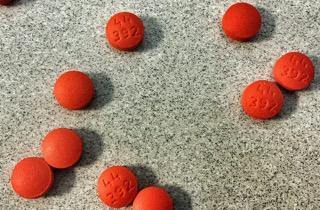Red round tablets with imprints on a speckled countertop, pain relief medicine concept
