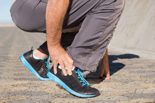 Person outdoors clutching painful ankle, possible sports injury or tendon discomfort