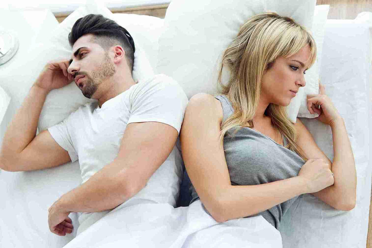 Sad couple lying in bed back to back looking stressed, relationship and wellness concept