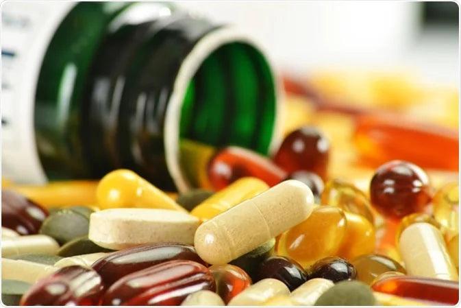 Assorted dietary supplement capsules and tablets spilling from a bottle